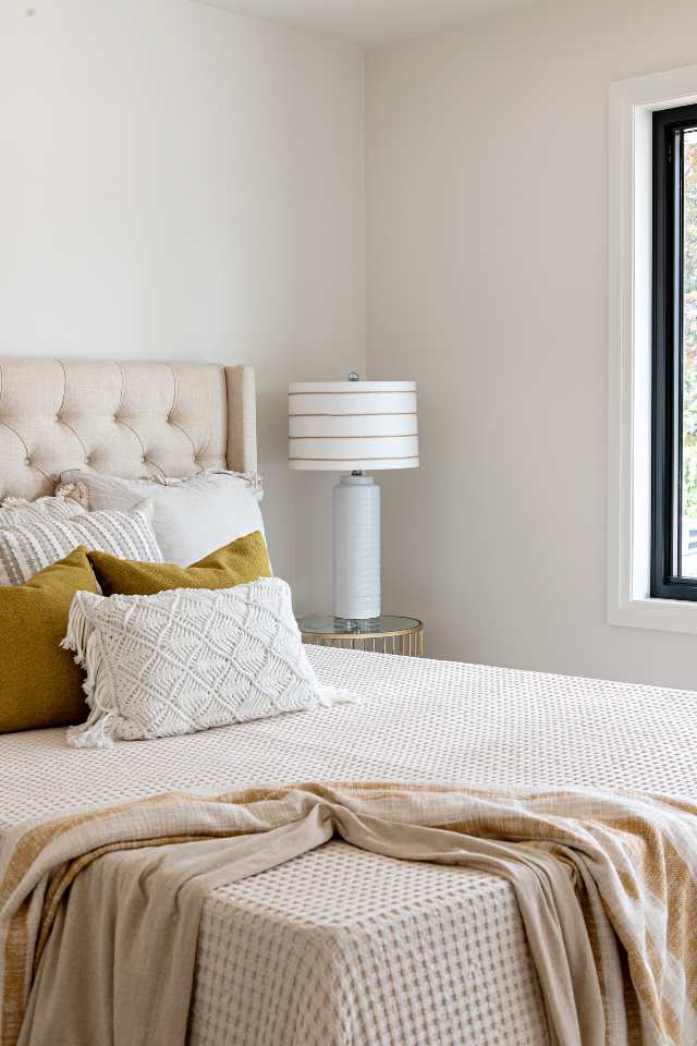 neutral bedding in primary suite with bedside lamp